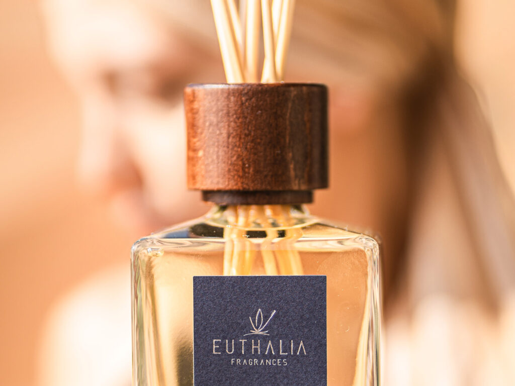 Diffusore di profumi Euthalia Fragrances Nefertiti Oud con bastoncini di legno su tavolo di legno, sfondo beige chiaro, design elegante e raffinato. Chi siamo. Il piacere delle vacanze - holidays pleasure