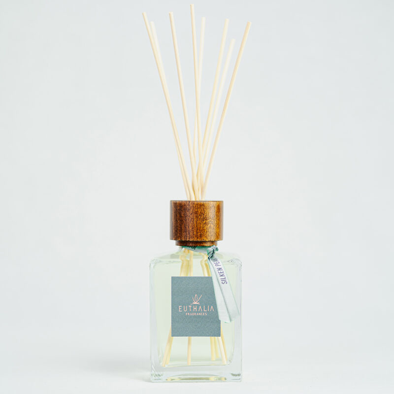Fragranza Silken Pear. Diffusore a bastoncini Euthalia Fragrances, con flacone in vetro trasparente. Il tappo in legno e i bastoncini completano il design elegante, ideale per profumare ambienti con una fragranza raffinata e di lunga durata.