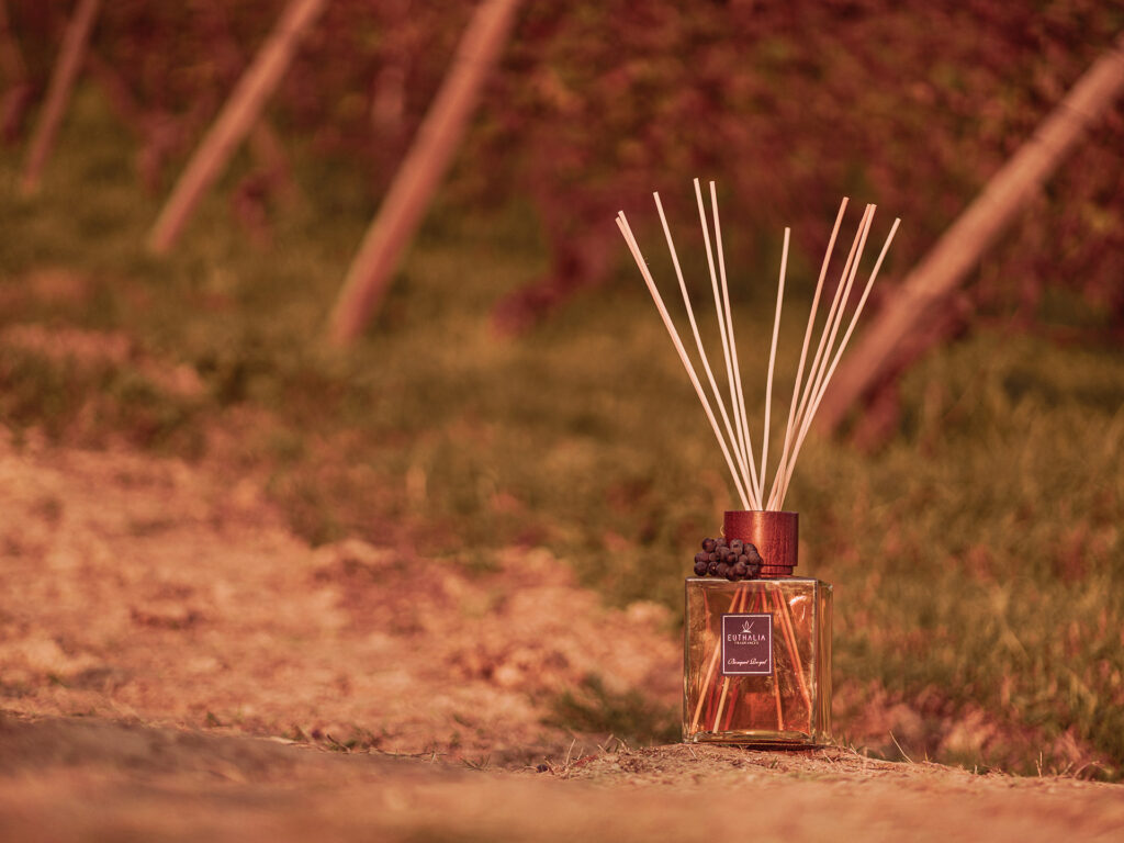 Diffusore a bastoncini Euthalia Fragrances Bouquet Royal posizionato tra i filari, immerso in una luce dorata che evoca il calore autunnale e un’atmosfera accogliente e raffinata.
