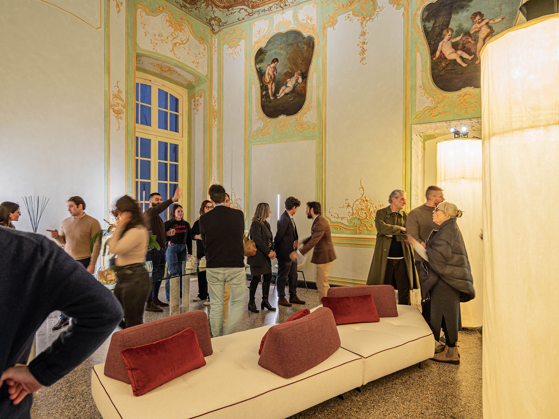 Immagine dell’inaugurazione del nuovo show-room Euthalia Fragrances nel salone affrescato di Palazzo Cosmo Centurione a Genova, con ospiti che interagiscono tra installazioni luminose e ambientazione storica. Image of the inauguration of the new Euthalia Fragrances showroom inside the frescoed hall of Palazzo Cosmo Centurione in Genoa, with guests interacting among lighting installations and the historic interior.