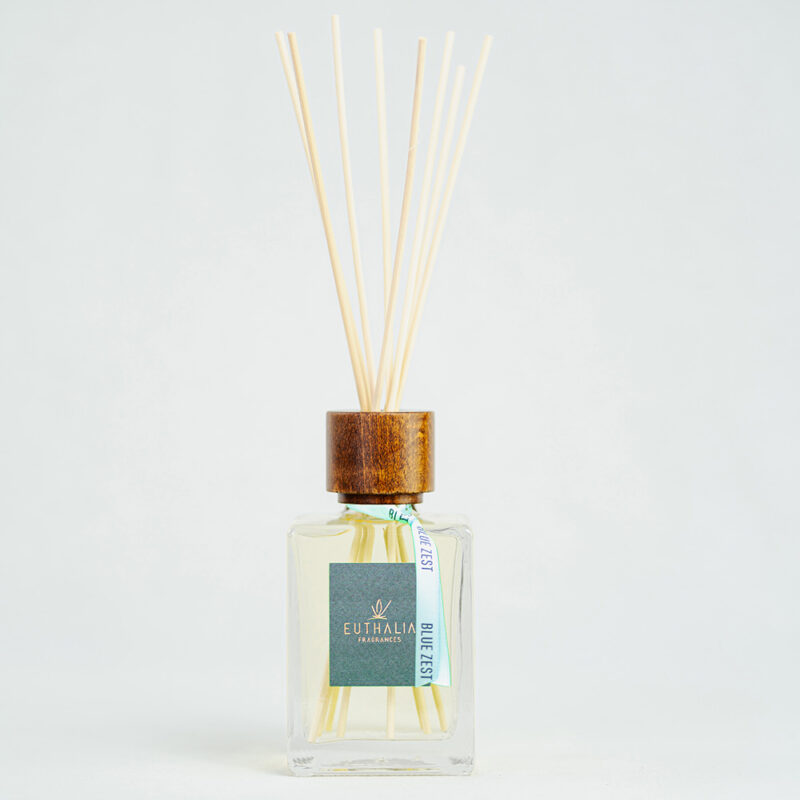 Fragranza Blue Zest. Diffusore a bastoncini Euthalia Fragrances, con flacone in vetro trasparente. Il tappo in legno e i bastoncini completano il design elegante, ideale per profumare ambienti con una fragranza raffinata e di lunga durata.