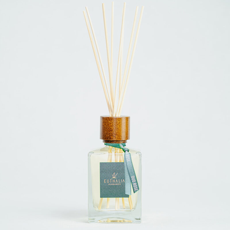 Fragranza Oud Rose. Diffusore a bastoncini Euthalia Fragrances, con flacone in vetro trasparente. Il tappo in legno e i bastoncini completano il design elegante, ideale per profumare ambienti con una fragranza raffinata e di lunga durata.