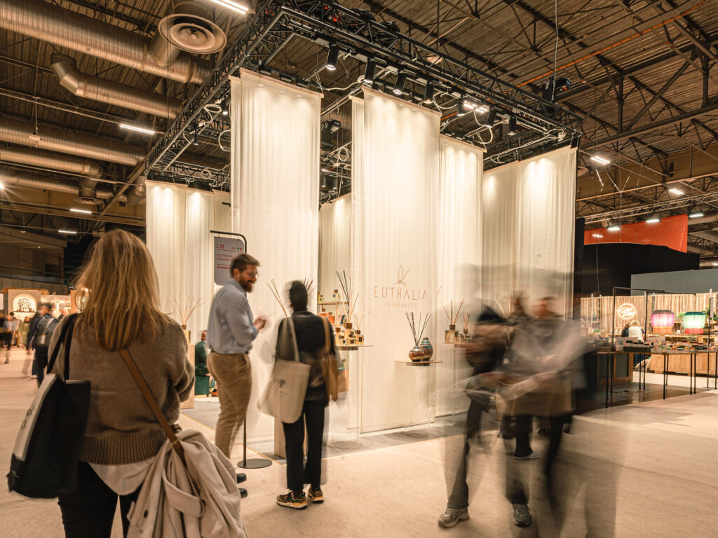 Inizio 2026: stand Euthalia Fragrances a Maison&Objet con tende bianche, esposizione di diffusori e visitatori in fiera. Start of 2026: Euthalia Fragrances booth at Maison&Objet with white drapes, diffuser display and visitors walking through the trade show.