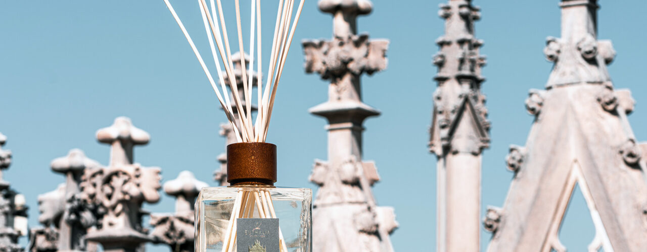 Diffusore Duomo Milano sul Duomo di Milano, tra guglie gotiche e cielo azzurro, ispirato al profumo della neve e all’atmosfera di Milano Cortina 2026. Duomo Milano reed diffuser on the Duomo rooftop in Milan, among Gothic spires and blue sky, inspired by the scent of snow and the atmosphere of Milan Cortina 2026.