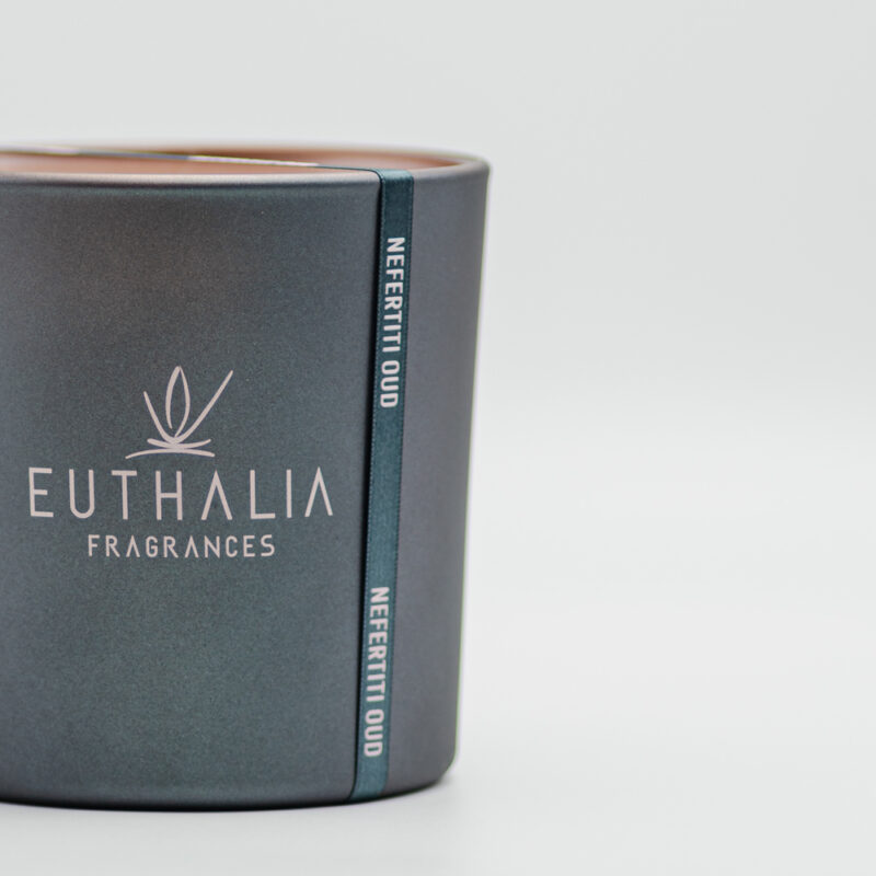 Candela profumata Nefertiti Oud Euthalia Fragrances in vaso antracite opaco con logo serigrafato, dettaglio elegante di design per la casa. Nefertiti Oud scented candle by Euthalia Fragrances in a matte anthracite vessel with printed logo, an elegant design detail for the home.
