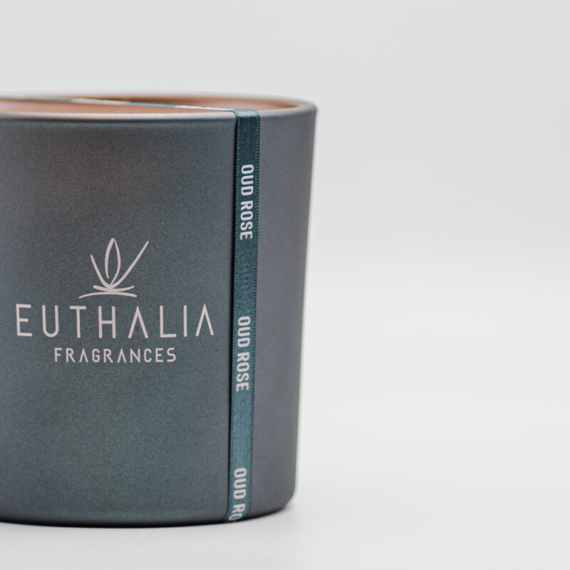 Candela profumata Oud Rose Euthalia Fragrances in vaso antracite opaco con logo serigrafato, dettaglio elegante di design per la casa. Oud Rose scented candle by Euthalia Fragrances in a matte anthracite vessel with printed logo, an elegant design detail for the home.